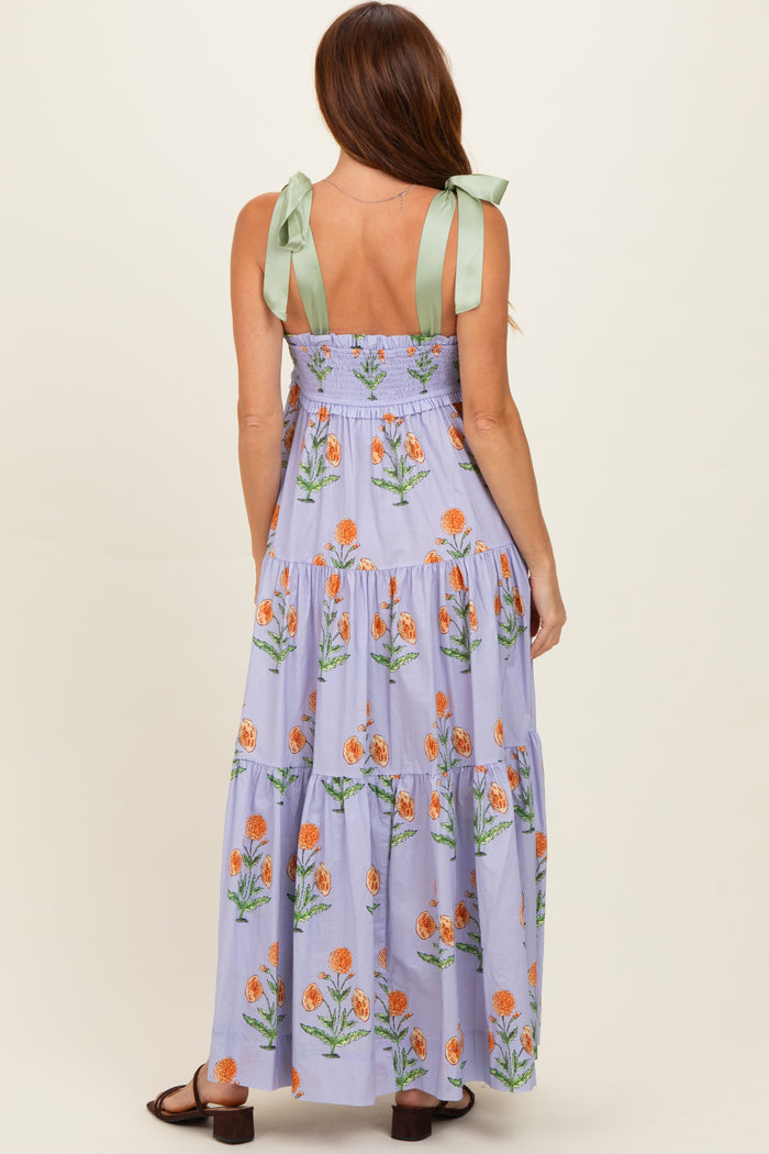 woman wearing a purple floral maxi dress with green tie straps, showing tiered design and back details