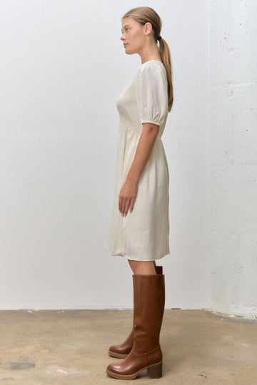woman wearing a cream short sleeve dress with puffed sleeves and knee-high brown boots