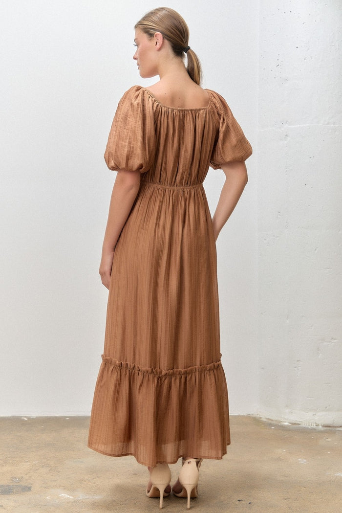 woman wearing a backview of a rust-colored maxi dress with puff sleeves and a tiered skirt