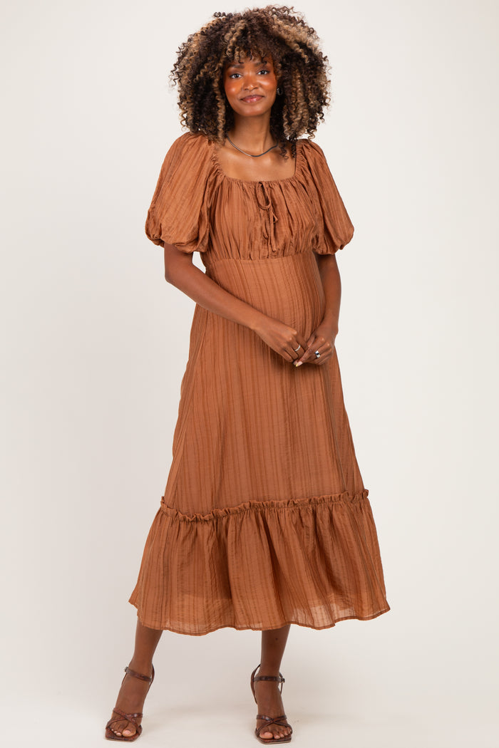 woman wearing a rust-colored maternity dress with balloon sleeves and a tiered hem, showing her baby bump