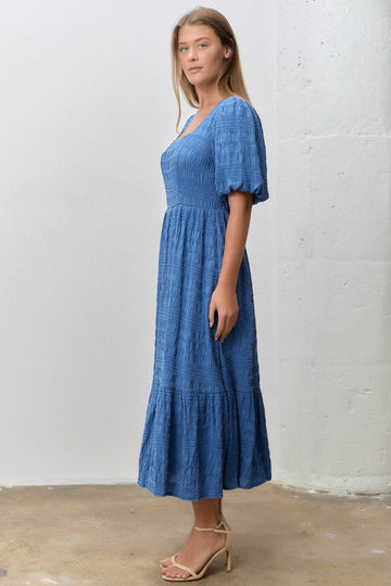 woman wearing a blue puff sleeve midi dress with a tiered skirt and a fitted bodice