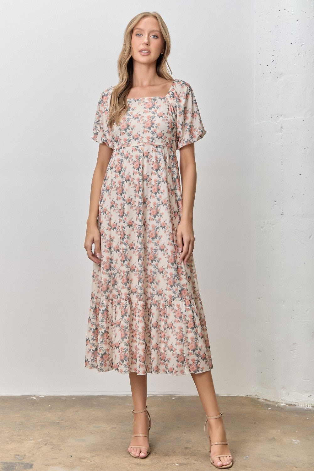 woman wearing a floral print midi dress with short sleeves and a square neckline, standing against a neutral background