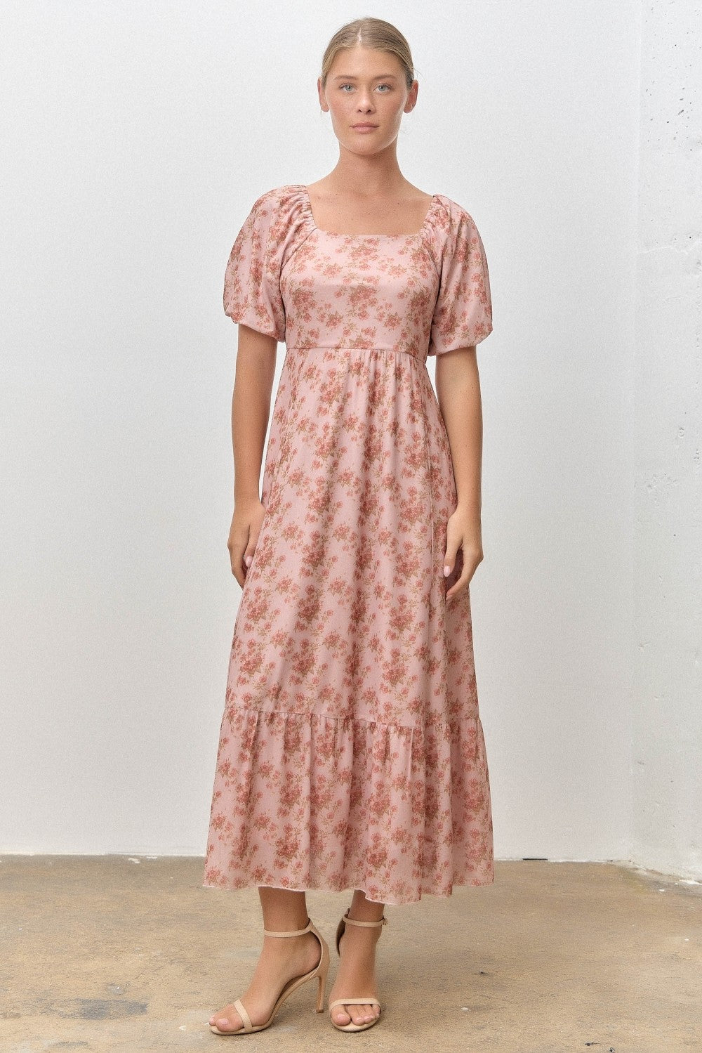woman wearing a pink floral maxi dress with puff sleeves and a tiered skirt, standing against a neutral background