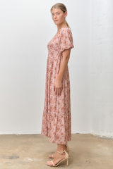 woman wearing a pink floral maxi dress with short puff sleeves and a tiered skirt, standing against a plain background