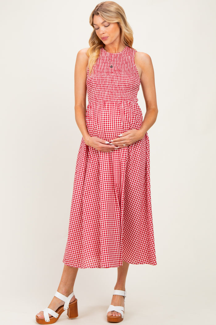 woman wearing a red and white gingham maternity dress with a smocked bodice and holding her baby bump