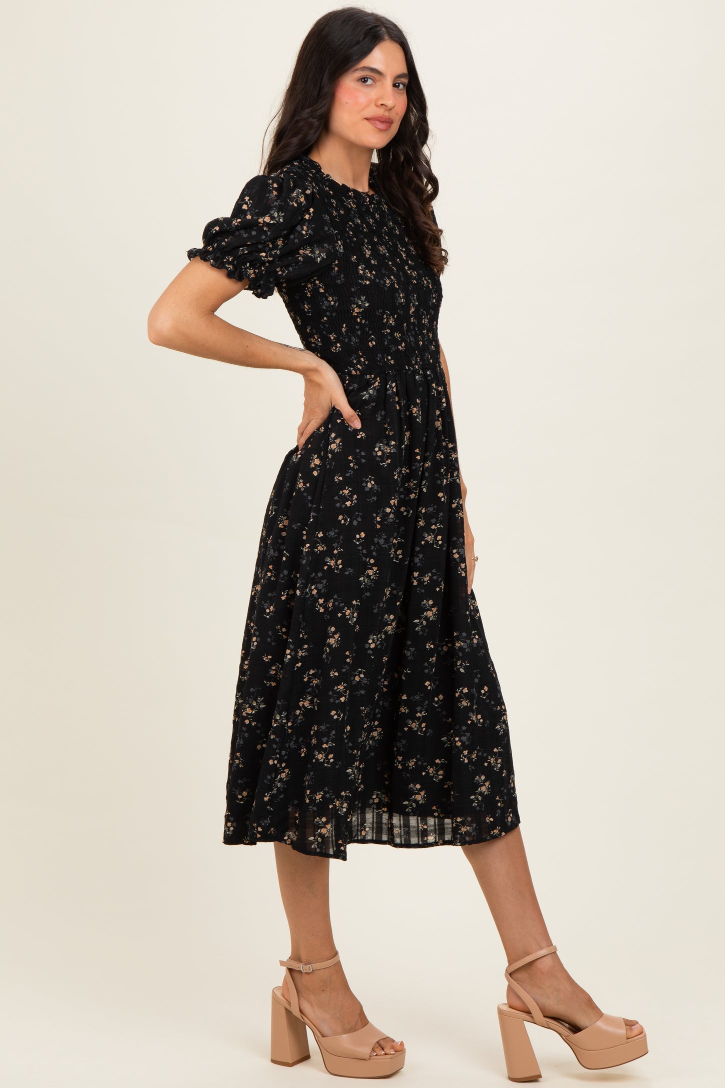 woman wearing a black floral midi dress with puff sleeves and a cinched waist, paired with nude platform heels