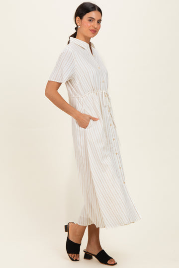 woman wearing a white and beige striped midi shirt dress with a tie waist and side pockets, standing in a relaxed pose