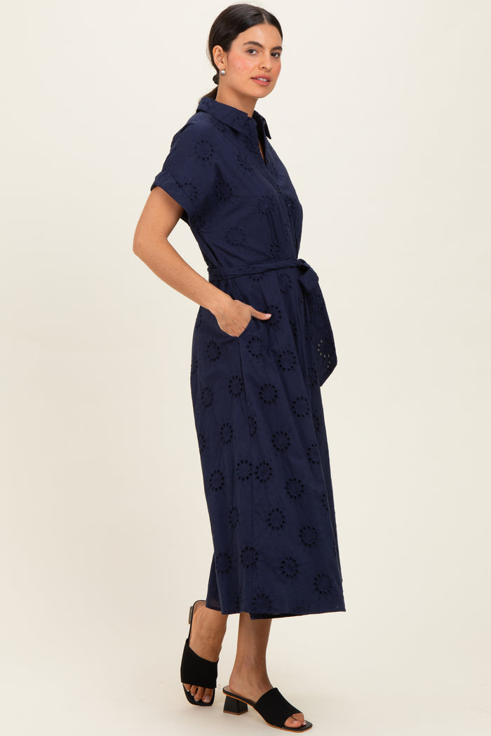 woman wearing a navy blue short sleeve button-up dress with an embroidered floral pattern and a tied waist belt
