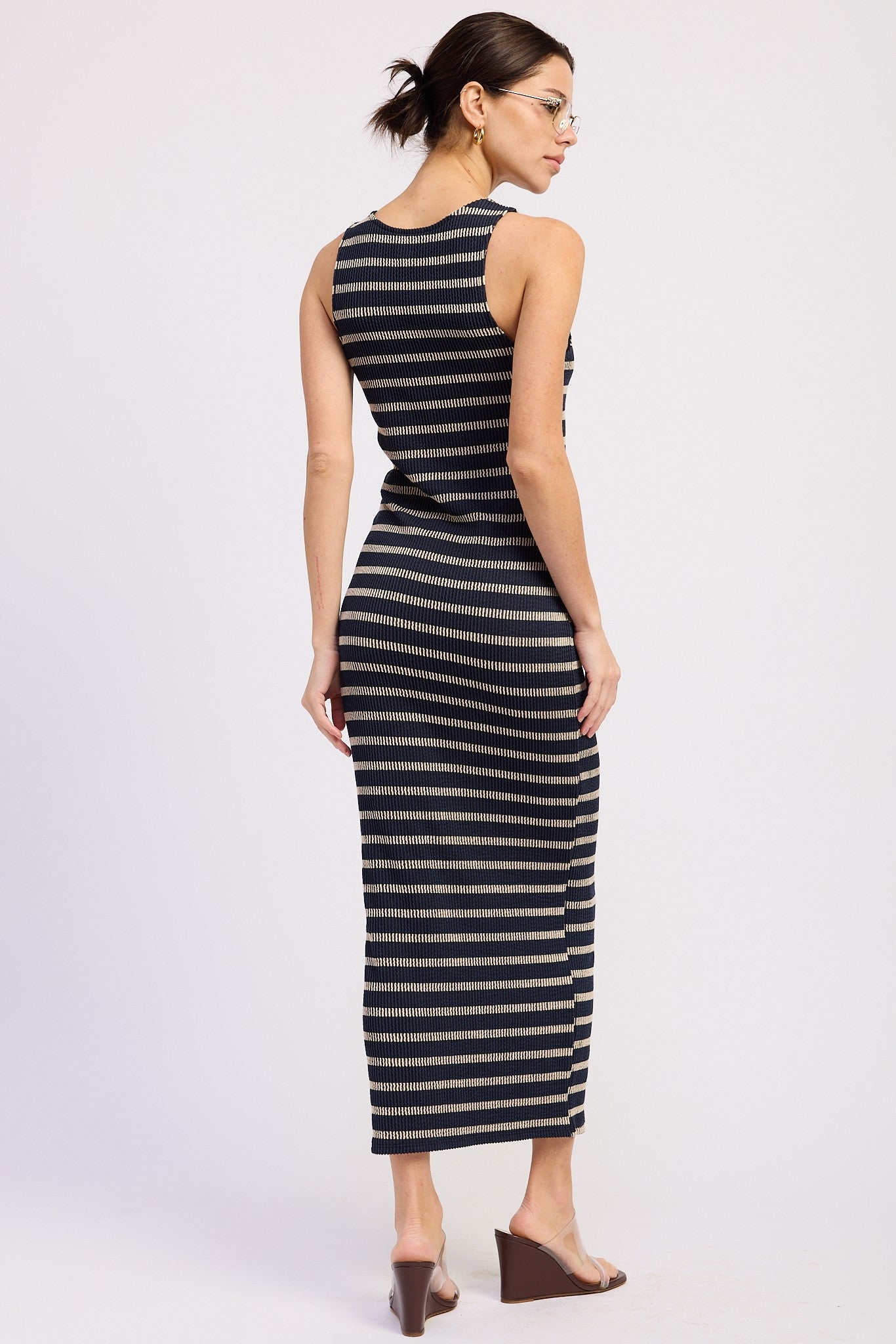 woman wearing a fitted black and beige striped maxi dress, showing the back and side details, with sleek brown heels