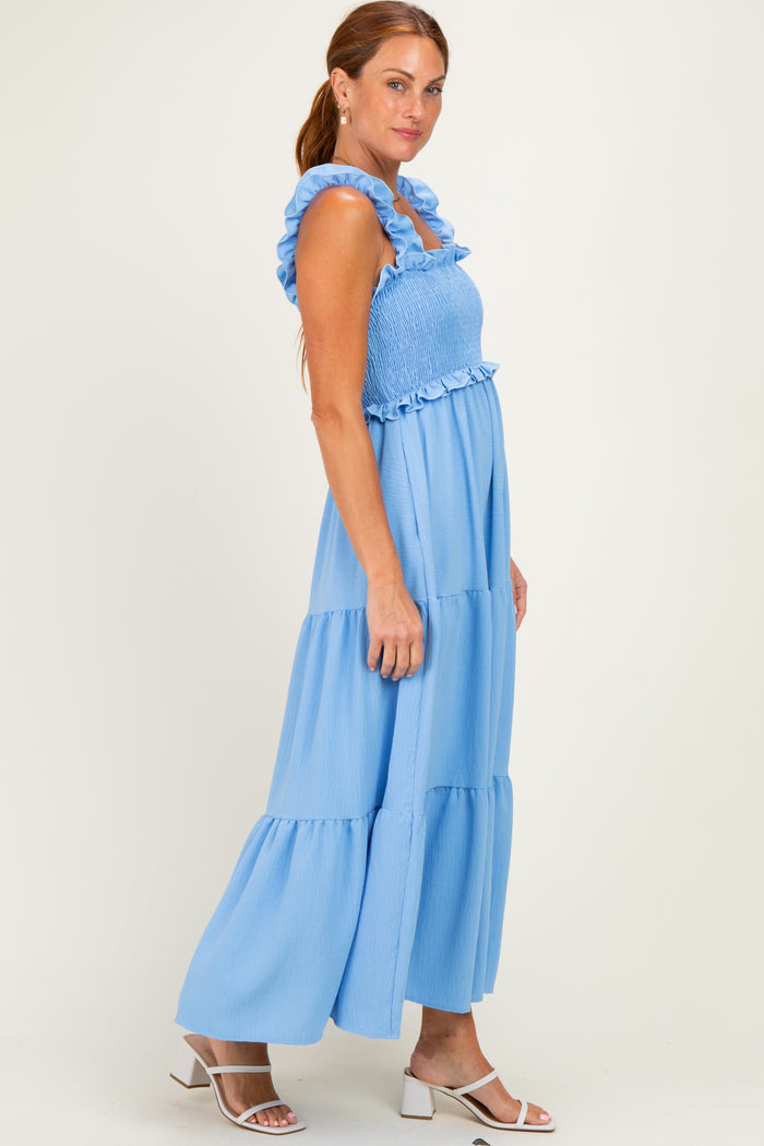 woman wearing a light blue maxi dress with smocked bodice and ruffled straps, standing in profile