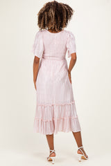 woman wearing a pink pleated maternity dress with puff sleeves and ruffle details, showing a side view of her baby bump