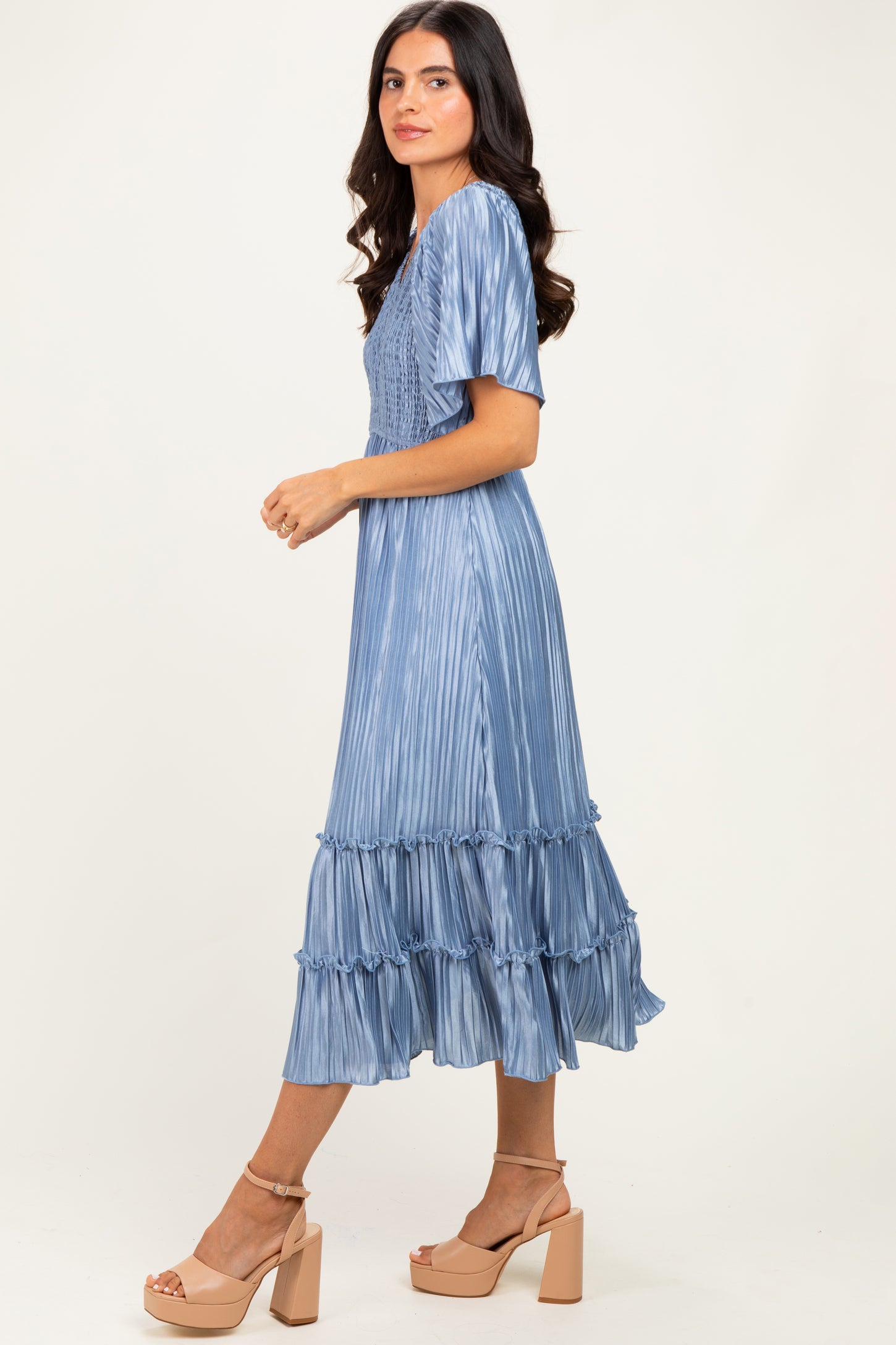 woman wearing a light blue pleated dress with ruffled tiers and short sleeves, styled with tan block heeled sandals