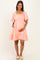 woman wearing a coral maternity dress with short puff sleeves, smocked bodice, and tiered ruffle skirt, holding her baby bump