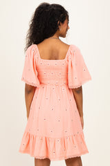 woman wearing a pink maternity dress with short sleeves, smocked bodice, and lace trim on the hem