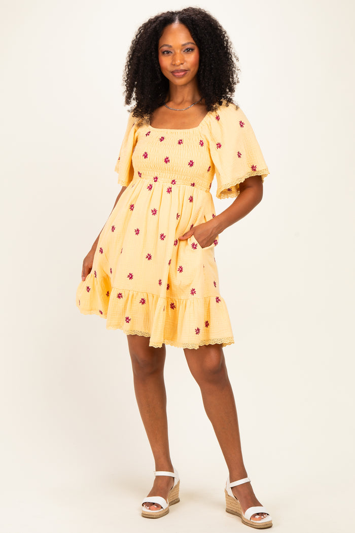 woman wearing a yellow floral print sundress with ruffled sleeves and pockets, standing in wedge sandals