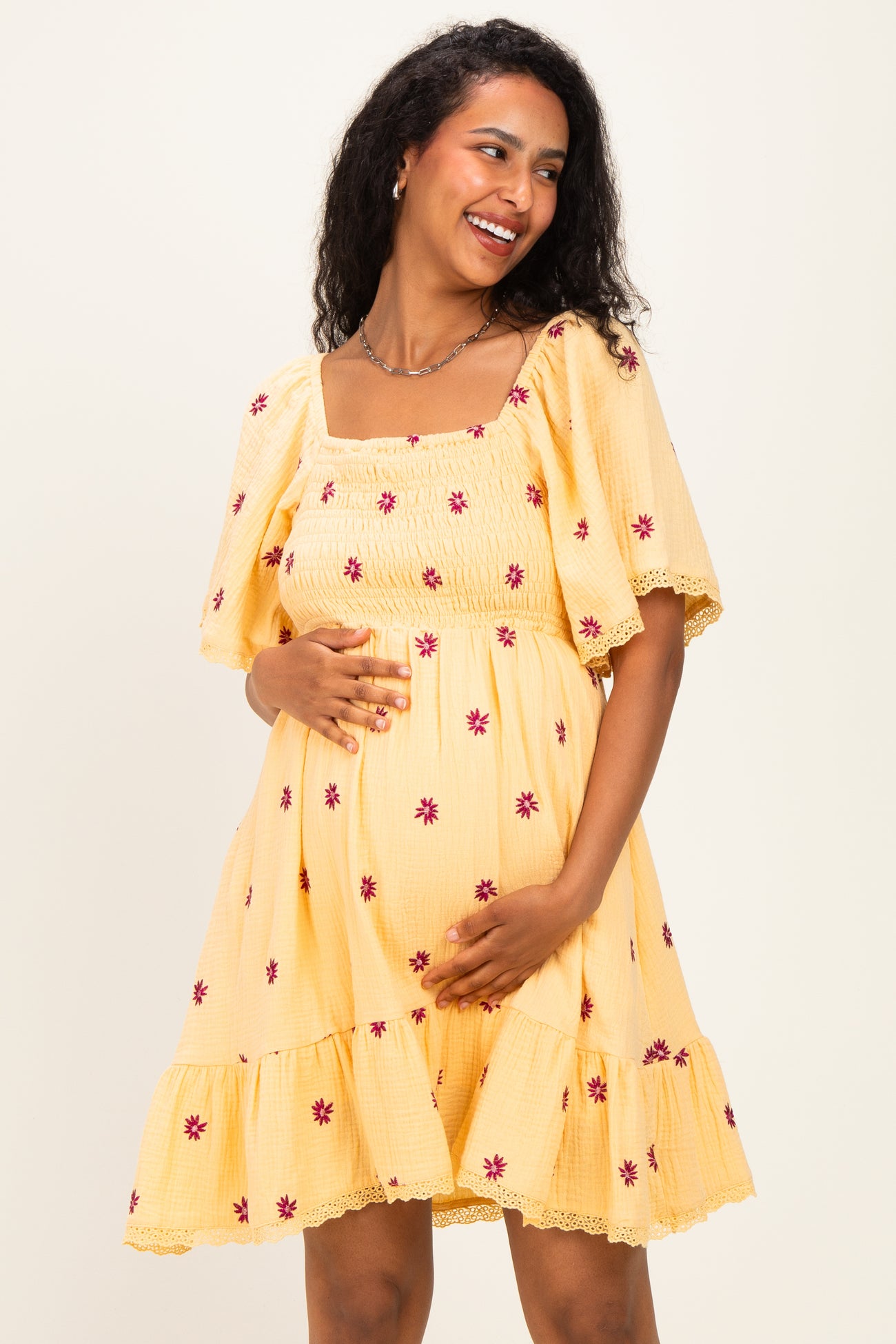 woman wearing a yellow short sleeve maternity dress with floral embroidery and a baby bump