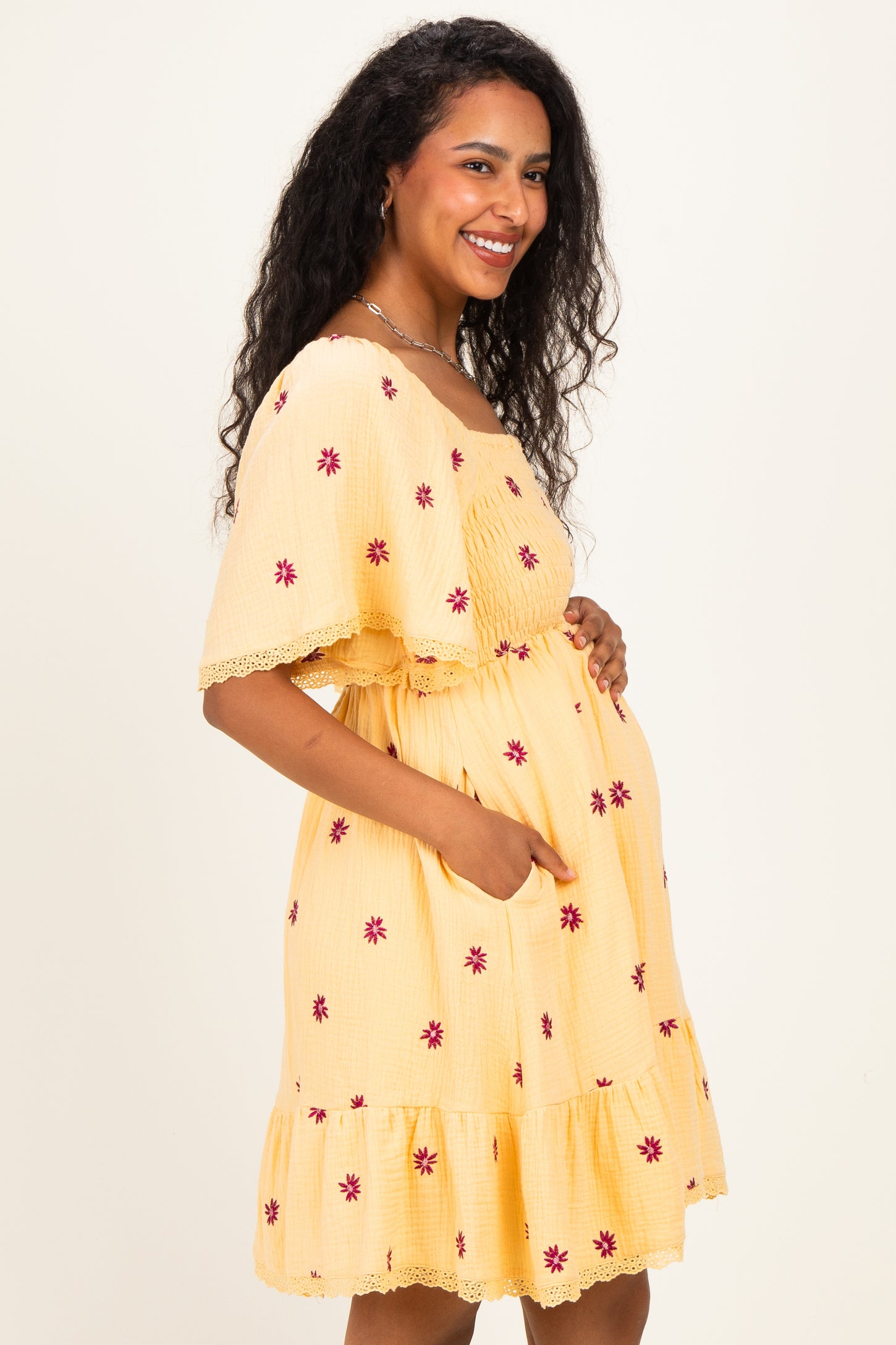 woman wearing a yellow maternity dress with floral embroidery and ruffle hem, showing her baby bump