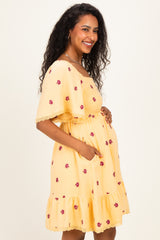 woman wearing a yellow maternity dress with floral embroidery and ruffle hem, showing her baby bump