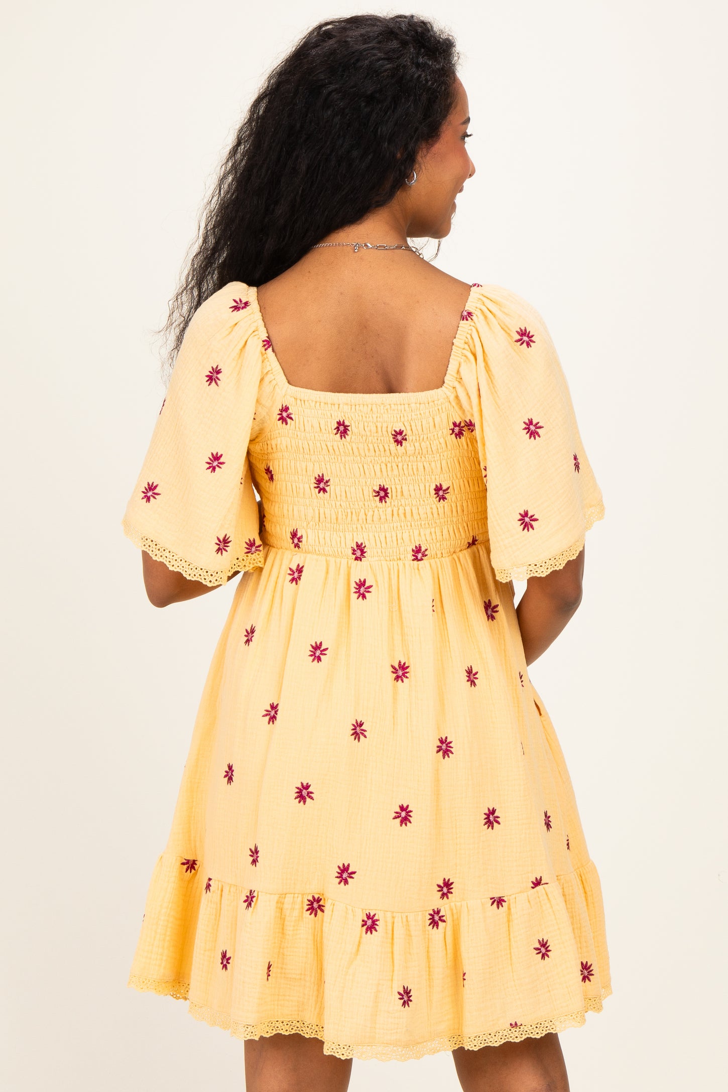 woman wearing a yellow floral embroidered maternity dress with a smocked back and ruffled hem