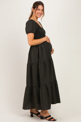 woman wearing a black and green gingham check maternity dress with short puff sleeves and a tiered skirt, cradling her baby bump