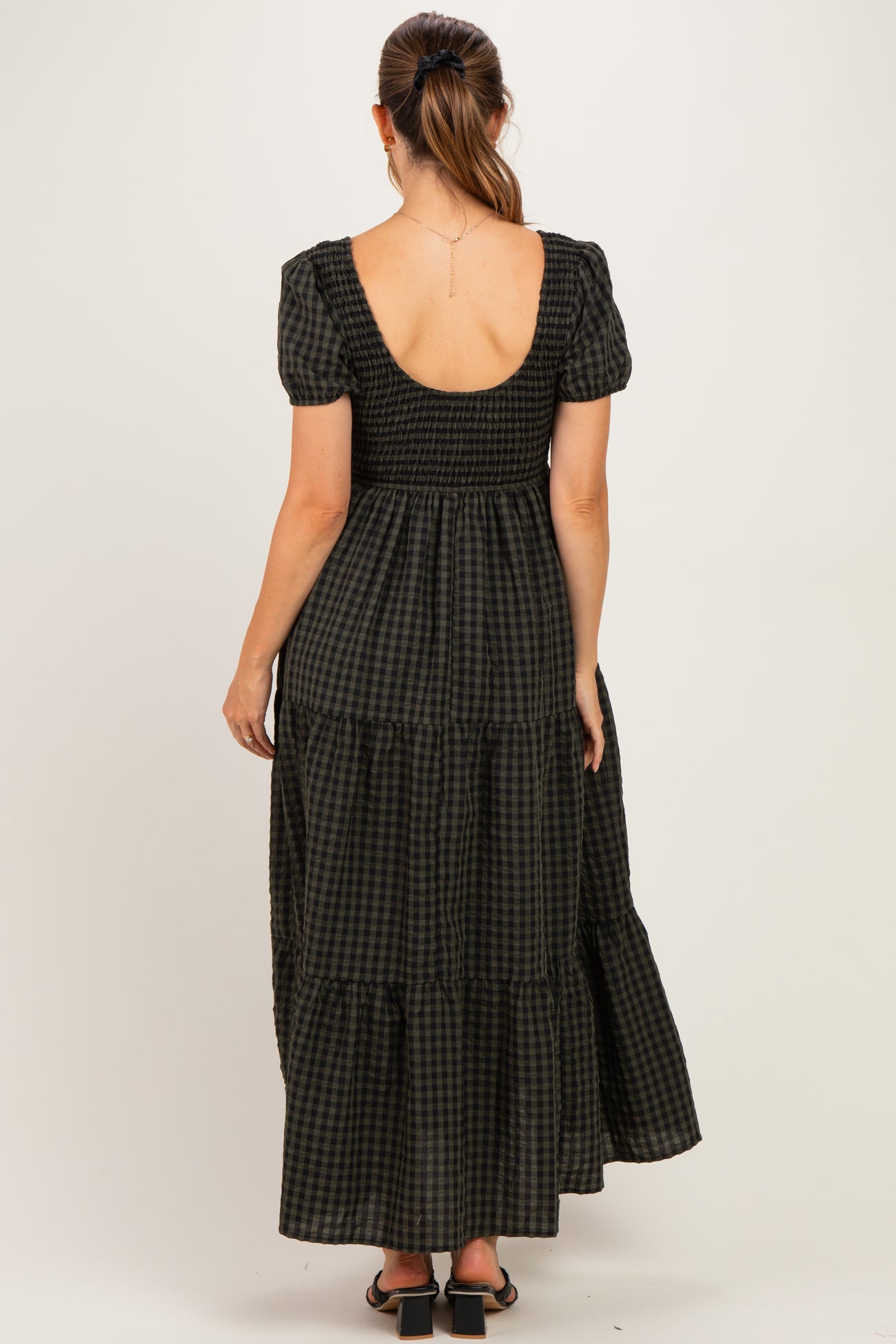 woman wearing a black and white checkered maternity maxi dress with a smocked bodice and short puff sleeves, showing her back