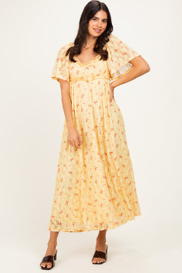woman wearing a yellow floral maxi dress with flutter sleeves and a layered design, standing against a neutral background