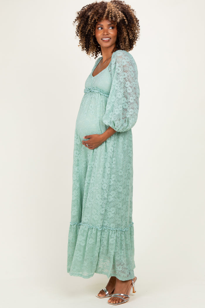 woman wearing a long mint green lace maternity dress with puff sleeves and a fitted bodice, showing her baby bump