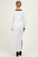 woman wearing a white long sleeve ribbed dress with a side slit and black trim, seen from the back