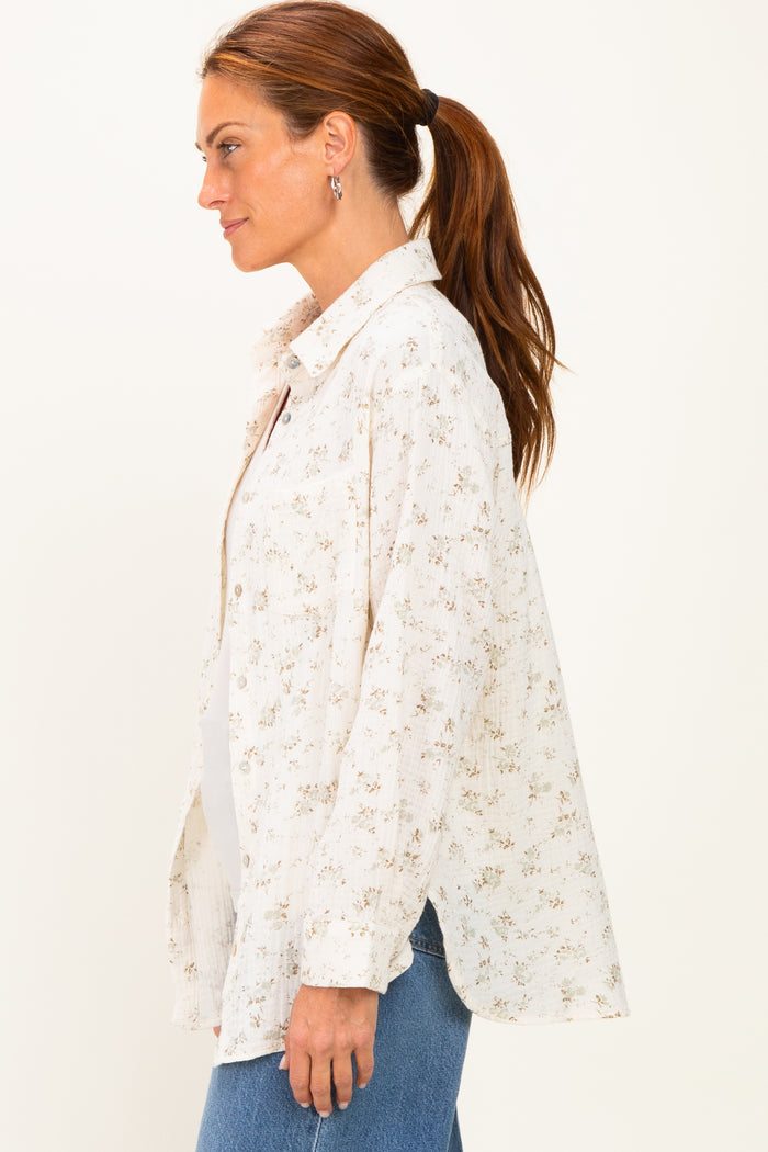 woman wearing a cream floral print button-up shirt with a loose fit and side slits, paired with blue jeans