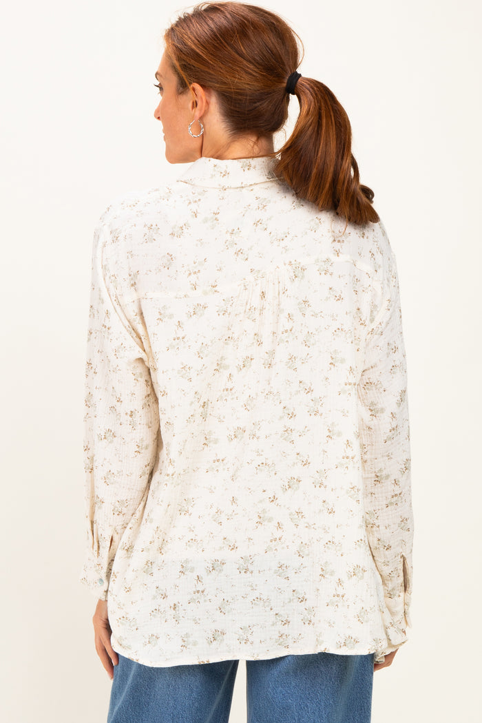 woman wearing a cream floral long sleeve blouse with a relaxed fit and button details, viewed from the back