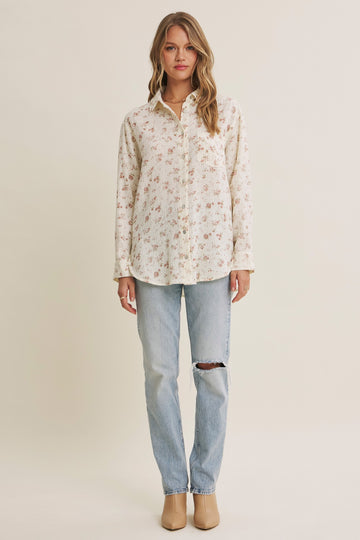 woman wearing a cream button-up shirt with floral print and light wash ripped jeans