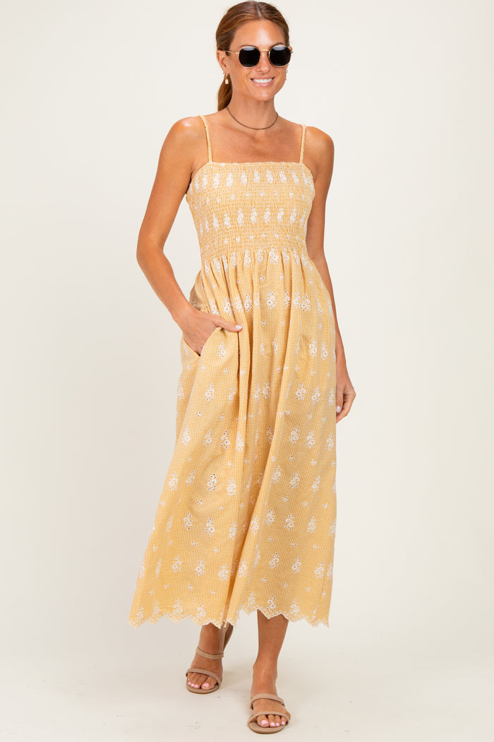 woman wearing a yellow smocked maxi dress with white floral patterns and pockets, paired with sunglasses and sandals