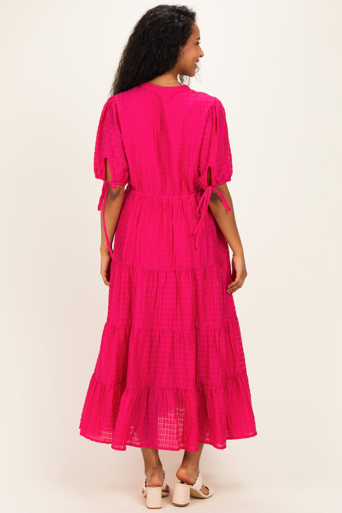 woman wearing a bright pink maternity maxi dress with tiered detailing and puff sleeves, showing a relaxed fit from the back