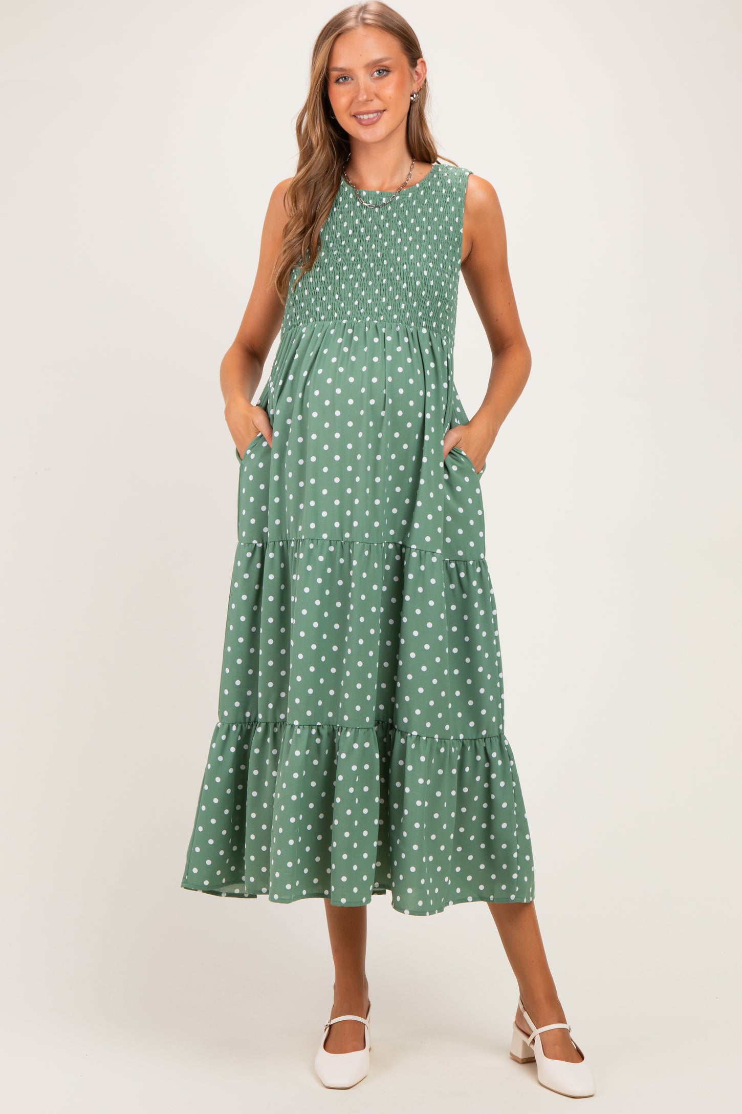 woman wearing a green polka dot maternity dress with smocking and tiers, featuring pockets and a flowing silhouette