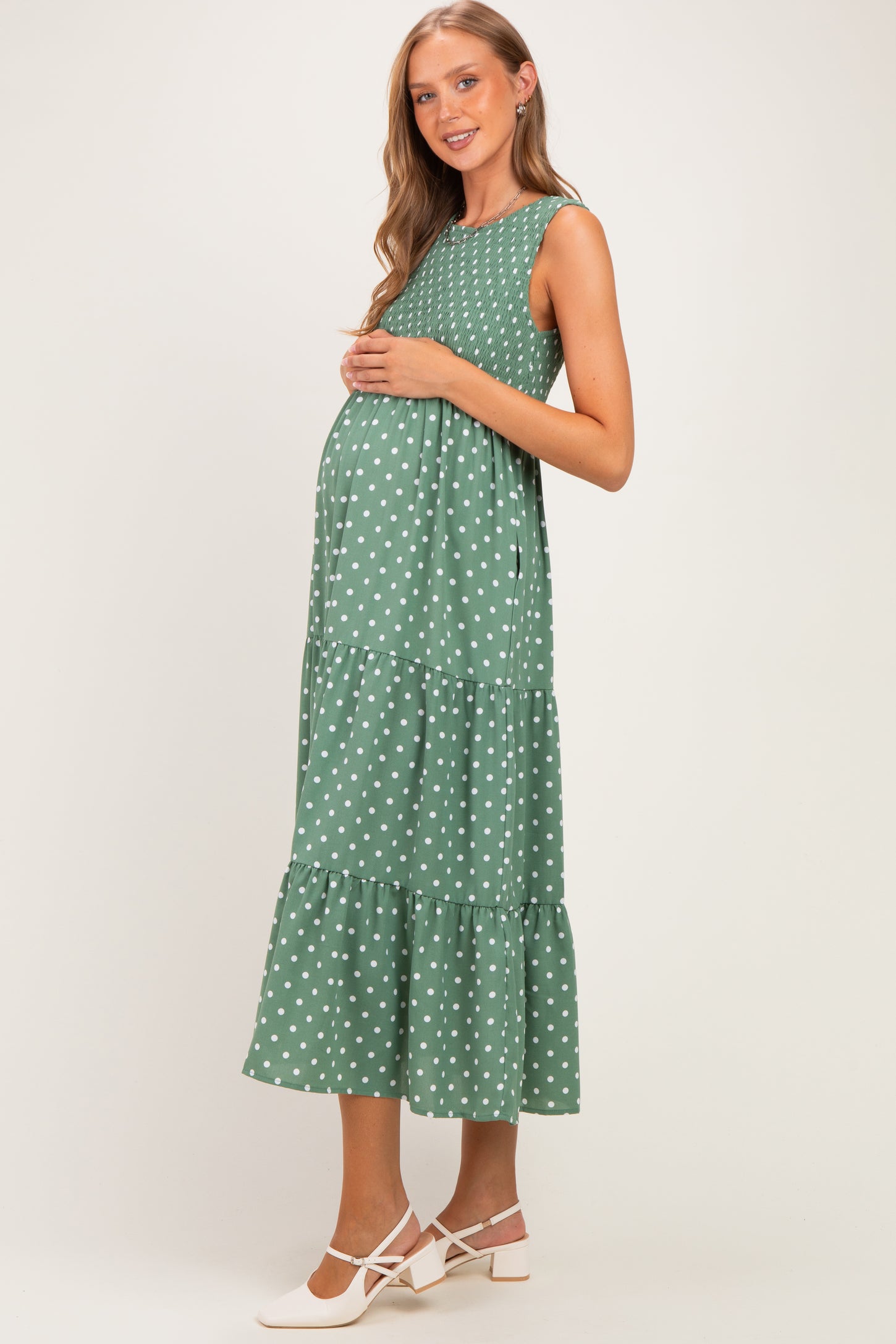 woman wearing a green polka dot maternity maxi dress and holding her baby bump