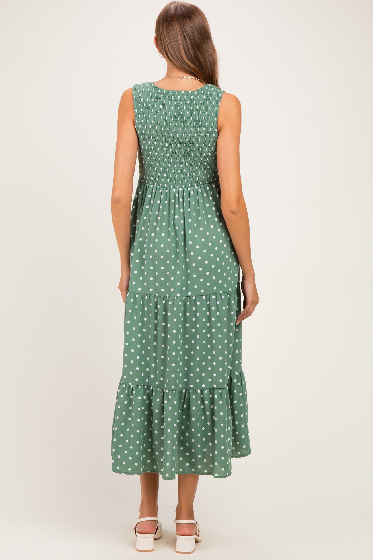 woman wearing a green polka dot maternity maxi dress with smocked bodice and tiered skirt, showing her back