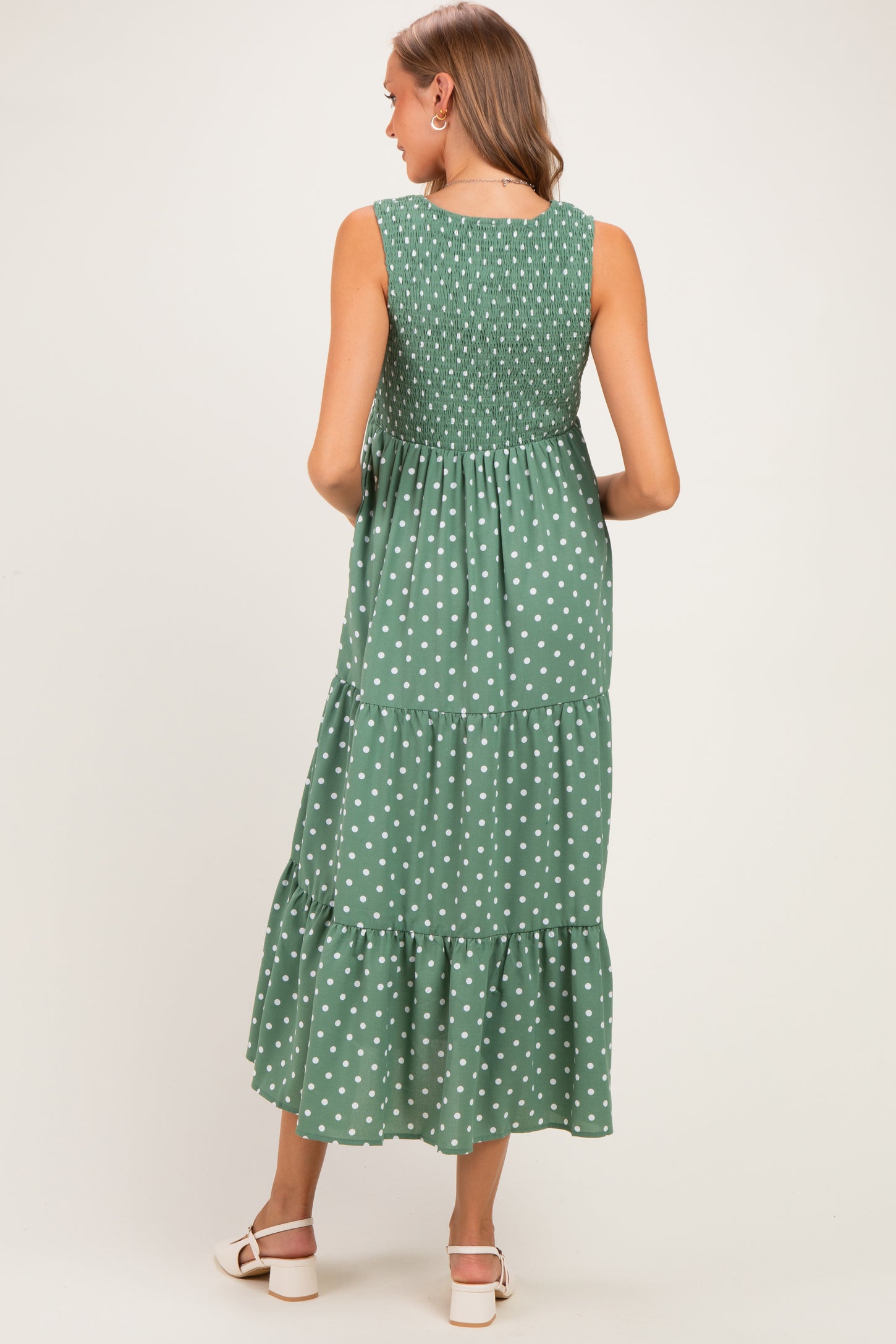 woman wearing a green polka dot maternity maxi dress with a smocked bodice and tiered skirt, viewed from the back
