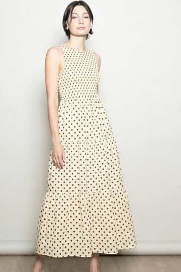woman wearing a sleeveless cream maxi dress with brown polka dots and a tiered skirt