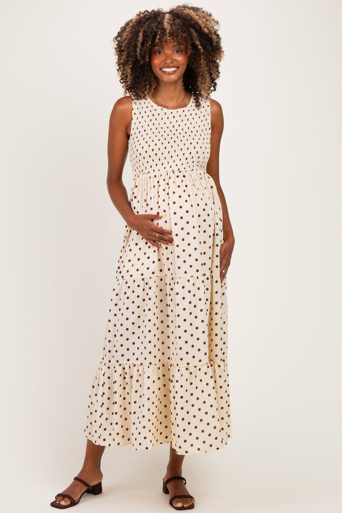 woman wearing a cream polka dot maternity dress with a tiered hem and holding her baby bump
