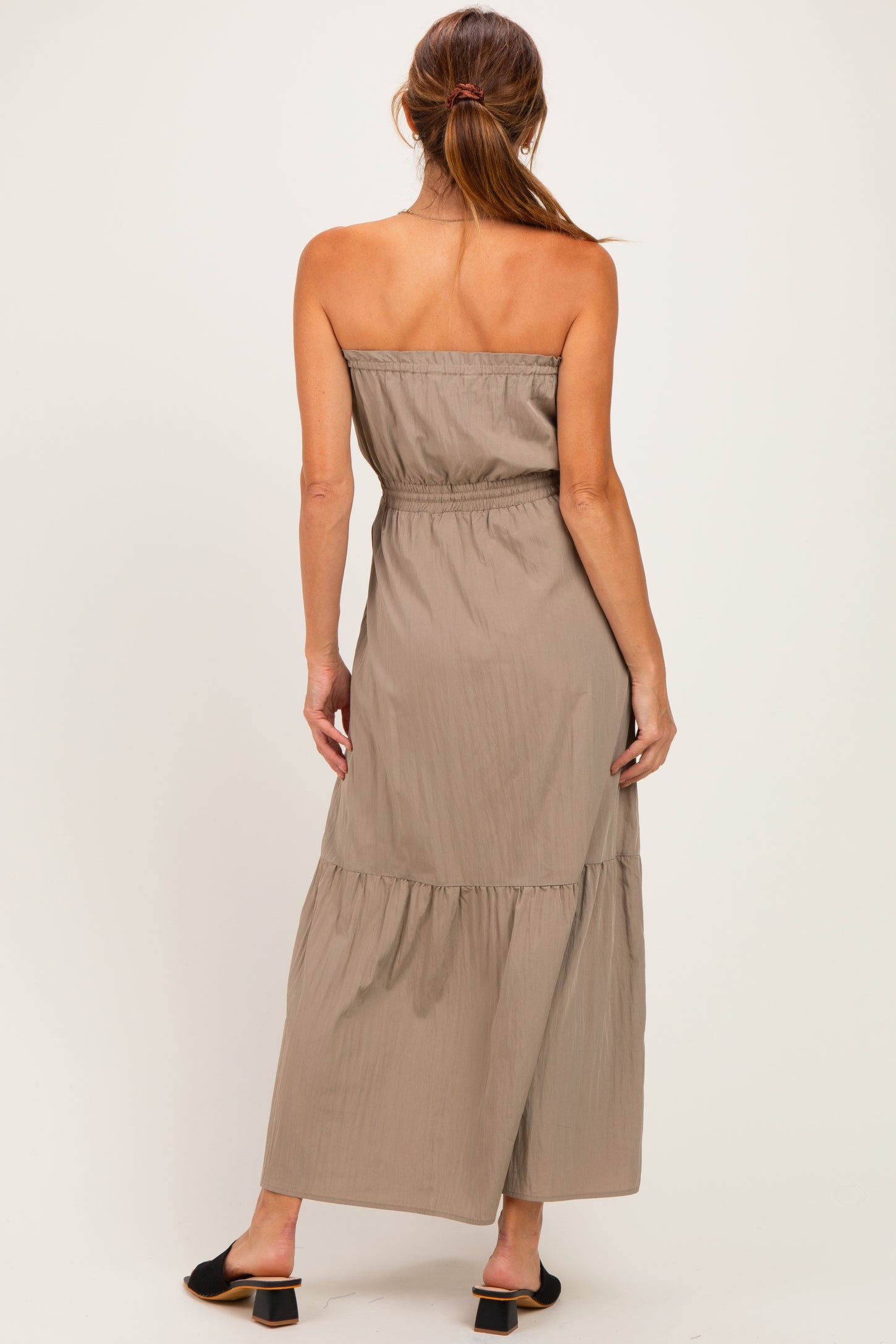 woman wearing a taupe strapless maxi dress with an elastic waist and tiered hem, shown from the back