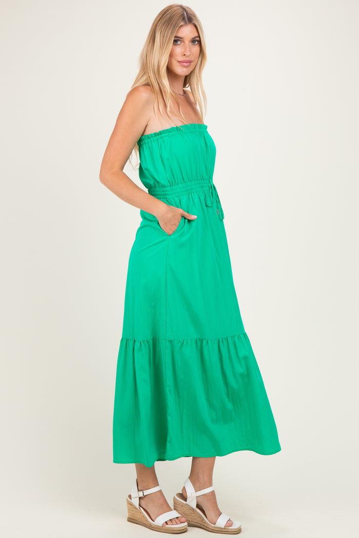 woman wearing a green strapless maxi dress with pockets and a tiered hem, paired with wedge sandals