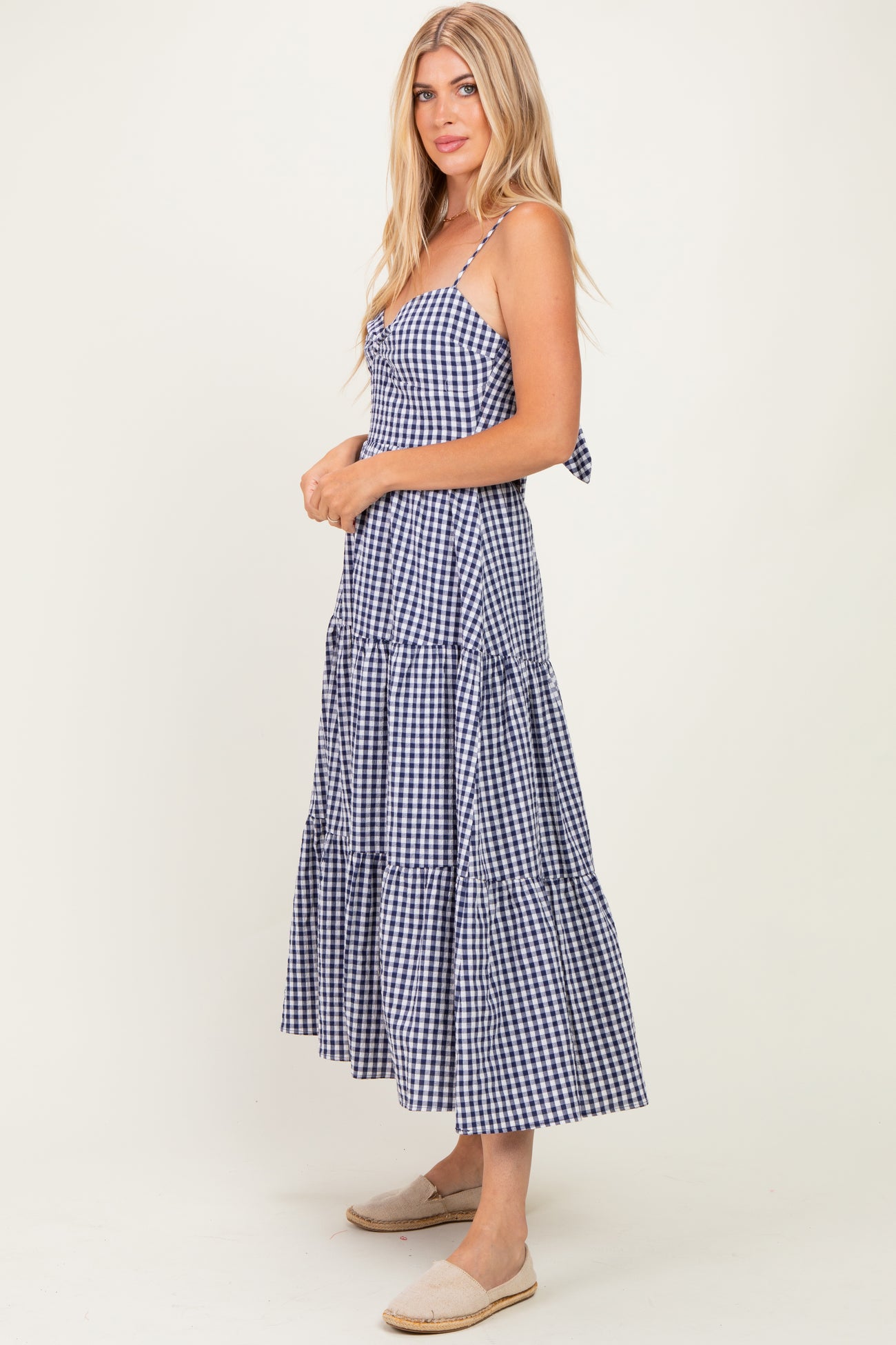 woman wearing a navy and white gingham tiered maxi dress with adjustable straps and a tied back detail
