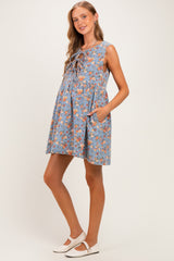 woman wearing a sleeveless blue floral maternity dress with a tie-front detail and pockets, showcasing her baby bump