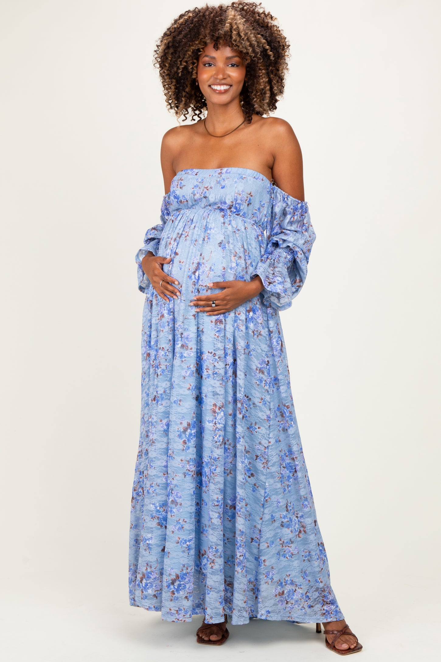 woman wearing a light blue off-the-shoulder floral maternity dress and cradling her baby bump