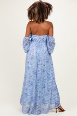 woman wearing a blue floral off-the-shoulder maternity dress with puffed sleeves and a flowing maxi length