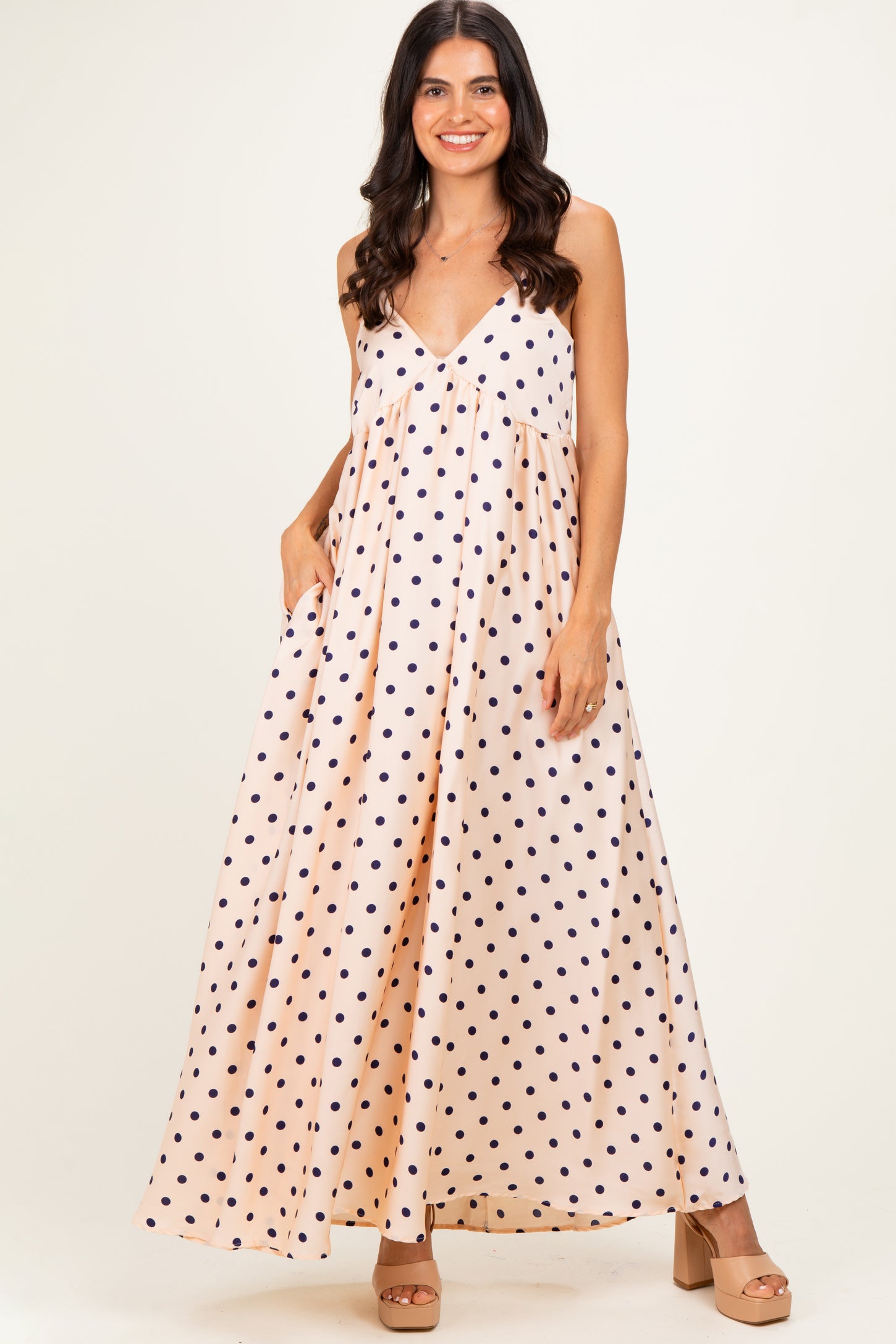 woman wearing a blush pink maxi dress with navy polka dots and pockets, styled with beige platform heels