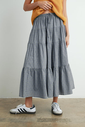 woman wearing a grey tiered maxi skirt with yellow patterns and paired with white sneakers and a mustard knit top