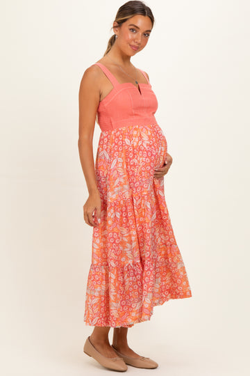 woman wearing a coral maternity dress with floral print and tiered skirt, showing her baby bump