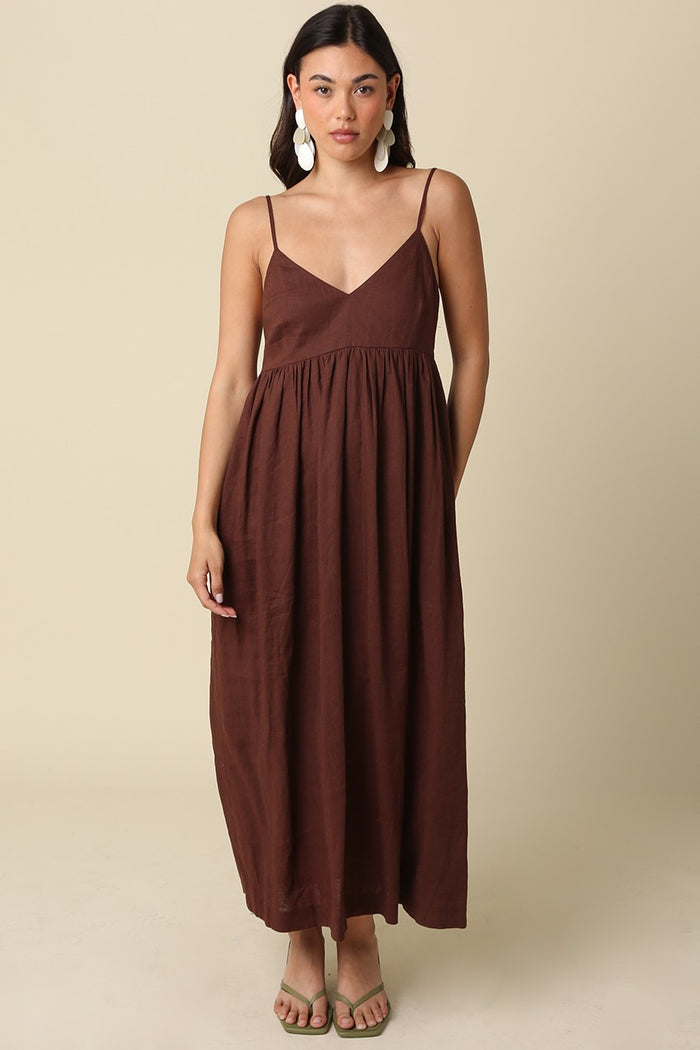 woman wearing a brown sleeveless maxi dress with a v-neckline and gathered waist, styled with green sandals