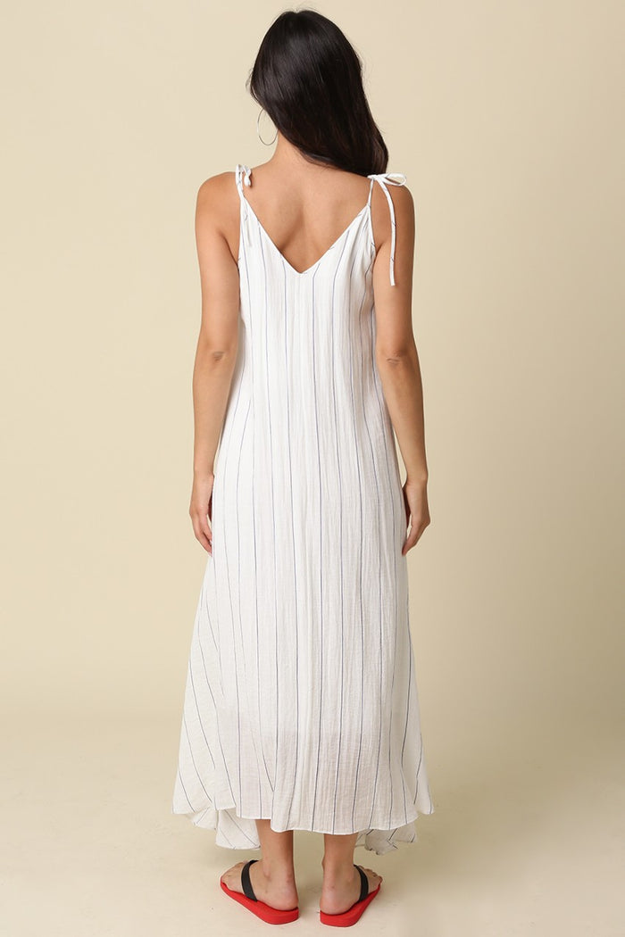 woman wearing a white striped maxi dress with tie straps and a flowing silhouette from the back